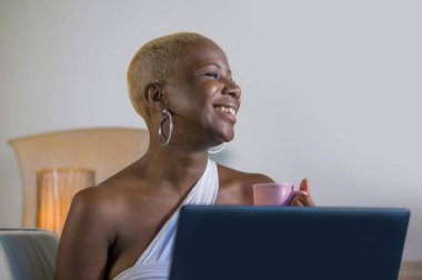 evde dizüstü bilgisayar üzerinde çalışan gülümseyen genç güzel mutlu siyah afro Amerikalı kadın girişimci bağımsız çalışma ve Internet serbest iş kanepe kanepede rahat