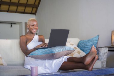 evde dizüstü bilgisayar üzerinde çalışan gülümseyen genç güzel mutlu siyah afro Amerikalı kadın girişimci bağımsız çalışma ve Internet serbest iş kanepe kanepede rahat