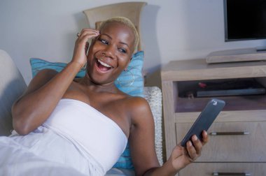 Genç güzel ve mutlu neşeli gülümseyen siyah afro Amerikalı kadın evde kanepe yalan rahat cep telefonunda kalma veya yaşam tarzı kavramında ağ Internet Sosyal medya app kullanarak