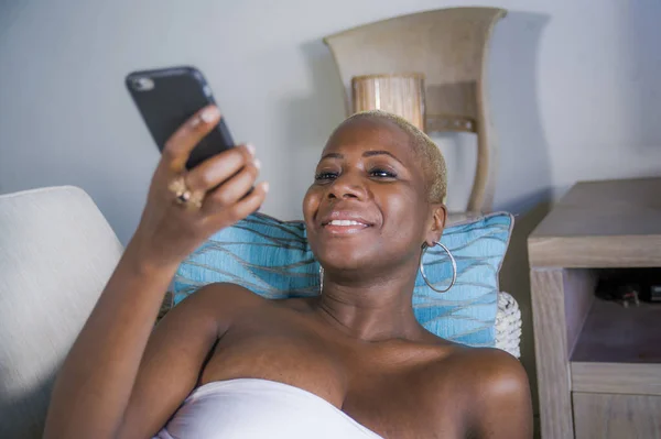 若く美しいと自宅のソファに横たわっている黒いアフロ アメリカ人女性は陽気な笑みを浮かべてリラックスしてください 幸せなデートまたはライフ スタイルのコンセプトでネットワークの携帯電話でインターネットのソーシャル メディア アプリを使用してください — ストック写真