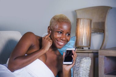 Genç güzel ve mutlu neşeli gülümseyen siyah afro Amerikalı kadın evde kanepe yalan rahat cep telefonunda kalma veya yaşam tarzı kavramında ağ Internet Sosyal medya app kullanarak