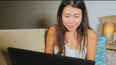 Genç güzel Asya öğrenci kız mutlu ve evde rahat koltuk kanepe üzerinde dizüstü bilgisayar ağ online teknoloji iletişim yaşam tarzı içinde neşeli internet kullanımı Çin 