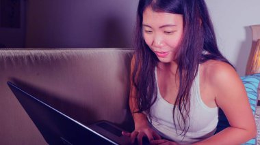 Genç güzel Asya öğrenci kız mutlu ve evde rahat koltuk kanepe üzerinde dizüstü bilgisayar ağ online teknoloji iletişim yaşam tarzı içinde neşeli internet kullanımı Çin 