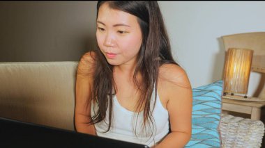 Genç güzel Asyalı Koreli öğrenci kız mutlu ve evde rahat koltuk kanepe üzerinde dizüstü bilgisayar ağ online teknoloji iletişim yaşam tarzı kavramı içinde neşeli internet kullanımı 