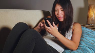 cep telefonu gülümseyen üzerinde Internet Sosyal medya app eğlence evde kanepe koltuk online iletişim yaşam tarzı kavramı içinde neşeli kullanarak genç tatlı mutlu ve güzel Asyalı Çinli kadın