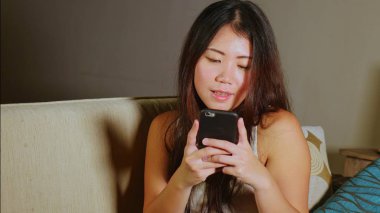 cep telefonu gülümseyen üzerinde Internet Sosyal medya app eğlence evde kanepe koltuk online iletişim yaşam tarzı kavramı içinde neşeli kullanarak genç tatlı mutlu ve güzel Asyalı Çinli kadın