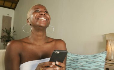 Genç güzel ve mutlu internet sosyal medya app üstünde hareket eden ağ ve online evde oturma odası koltuk kanepe oturup kalma telefon kullanarak siyah Afrikalı-Amerikalı kadın gülümseyen heyecan