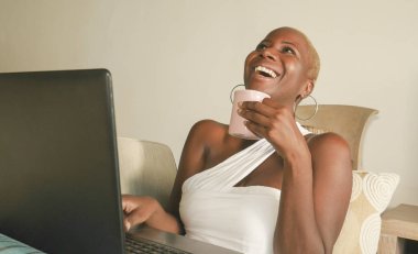 heyecanlı gülümseyen genç güzel ve mutlu siyah afro Amerikalı kadın dizüstü bilgisayar evde oturma odası kanepe blogger ve etkileyen yaşam tarzı rahat sosyal medya kullanarak Internet üzerinde eğleniyor