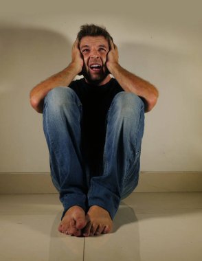 Genç umutsuz ve depresif adam tek başına evde oturan üzgün ve sinirli seyir stüdyo gölgeli ve dramatik ışık yerde ağlamaya üzüntü kavramı sorun ağrı ve depresyon acı