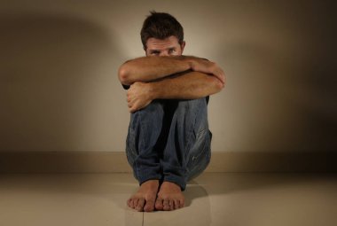 Genç umutsuz ve depresif adam tek başına evde oturan üzgün ve sinirli seyir stüdyo gölgeli ve dramatik ışık yerde ağlamaya üzüntü kavramı sorun ağrı ve depresyon acı