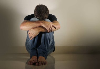 Genç umutsuz ve depresif adam tek başına evde oturan üzgün ve sinirli seyir stüdyo gölgeli ve dramatik ışık yerde ağlamaya üzüntü kavramı sorun ağrı ve depresyon acı