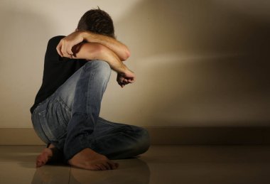 Genç umutsuz ve depresif adam tek başına evde oturan üzgün ve sinirli seyir stüdyo gölgeli ve dramatik ışık yerde ağlamaya üzüntü kavramı sorun ağrı ve depresyon acı