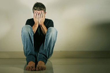 Genç umutsuz ve depresif adam tek başına evde oturan üzgün ve sinirli seyir stüdyo gölgeli ve dramatik ışık yerde ağlamaya üzüntü kavramı sorun ağrı ve depresyon acı