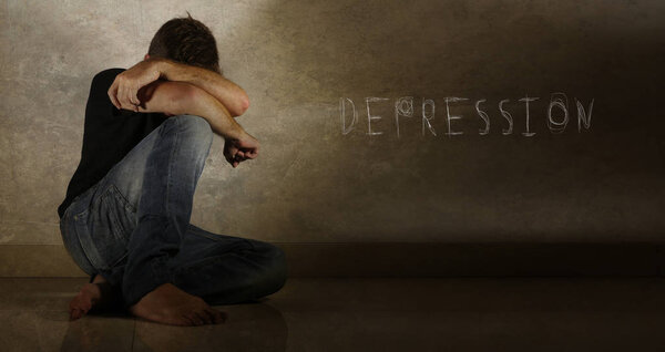 young desperate and depressed man crying alone sitting at home floor in shady and dramatic grunge isolated background sad and frustrated with the word depression written on the wall