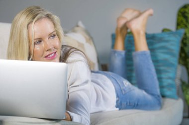 güzel ve mutlu sarışın kadın erken 40s evde oturma odası modern daire koltuk kanepe yaşam tarzı kavram, kanepe kanepede dizüstü çalışma yalan üzerinde rahat internet kullanımı rahat