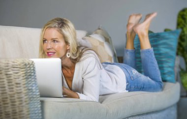 güzel ve mutlu sarışın kadın erken 40s evde oturma odası modern daire koltuk kanepe yaşam tarzı kavram, kanepe kanepede dizüstü çalışma yalan üzerinde rahat internet kullanımı rahat