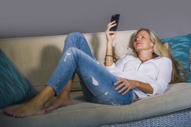 güzel ve mutlu sarışın kadın erken 40s evde oturma odası koltuk kanepe yaşam tarzı kavram rahat yatan gülümseyen cep telefonunda internet sosyal medya app kullanarak rahat