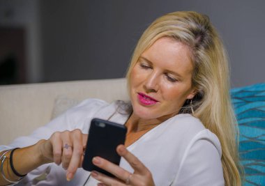 güzel ve mutlu sarışın kadın erken 40s evde oturma odası koltuk kanepe yaşam tarzı kavram rahat yatan gülümseyen cep telefonunda internet sosyal medya app kullanarak rahat