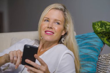 güzel ve mutlu sarışın kadın erken 40s evde oturma odası koltuk kanepe yaşam tarzı kavram rahat yatan gülümseyen cep telefonunda internet sosyal medya app kullanarak rahat