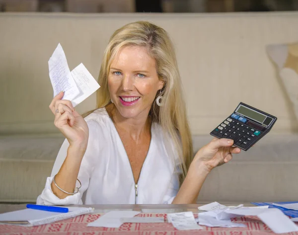 mutlu ve güzel 40 yaşlarında sarışın bir kadın gülümseyerek rahat başarılı yerli para gelir ve hesap makinesi ile kanepede muhasebe mali aylık iş pozitif dengesi hesaplama