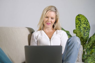 güzel ve mutlu zarif sarışın kadın erken 40s evde oturma odası dizüstü bilgisayar çalışma rahat kanepe kanepede yaşam tarzı kavram modern daire, internet kullanımı rahat