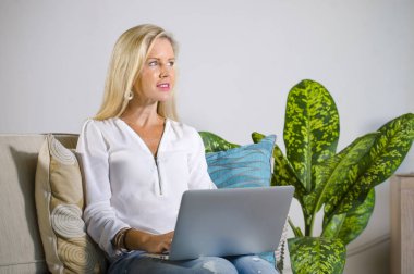 güzel ve mutlu zarif sarışın kadın erken 40s evde oturma odası dizüstü bilgisayar çalışma rahat kanepe kanepede yaşam tarzı kavram modern daire, internet kullanımı rahat