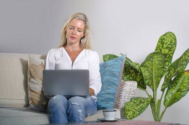 güzel ve mutlu zarif sarışın kadın erken 40s evde oturma odası dizüstü bilgisayar çalışma rahat kanepe kanepede yaşam tarzı kavram modern daire, internet kullanımı rahat