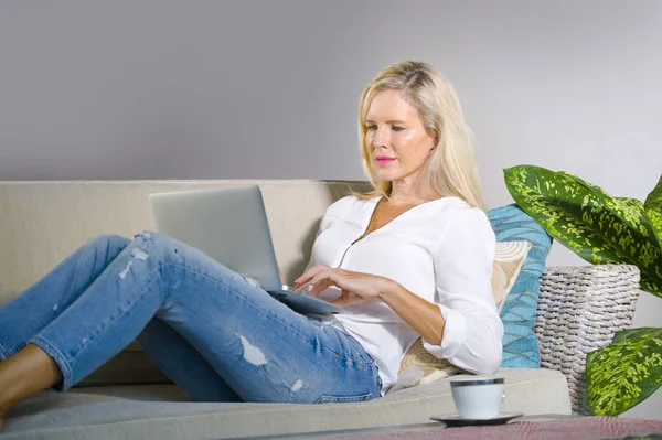 güzel ve mutlu zarif sarışın kadın erken 40s evde oturma odası dizüstü bilgisayar çalışma rahat kanepe kanepede yaşam tarzı kavram modern daire, internet kullanımı rahat