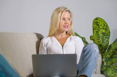 güzel ve mutlu zarif sarışın kadın erken 40s evde oturma odası dizüstü bilgisayar çalışma rahat kanepe kanepede yaşam tarzı kavram modern daire, internet kullanımı rahat