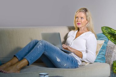 güzel ve mutlu zarif sarışın kadın erken 40s evde oturma odası dizüstü bilgisayar çalışma rahat kanepe kanepede yaşam tarzı kavram modern daire, internet kullanımı rahat