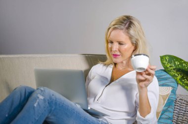 güzel ve mutlu zarif sarışın kadın erken 40s evde oturma odası dizüstü bilgisayar çalışma rahat kanepe kanepede yaşam tarzı kavram modern daire, internet kullanımı rahat