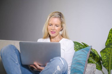 güzel ve mutlu zarif sarışın kadın erken 40s evde oturma odası dizüstü bilgisayar çalışma rahat kanepe kanepede yaşam tarzı kavram modern daire, internet kullanımı rahat
