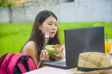 Açık havada çalışan genç çekici ve mutlu Asya Kore Dijital göçebe gibi online sosyal medya blogger seyahat başarı iş sağlıklı salata yemek dizüstü bilgisayar ile rahat