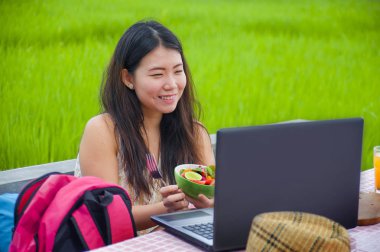 Açık havada çalışan genç çekici ve mutlu Asya Kore Dijital göçebe gibi internet sosyal medya blogger seyahat başarı iş sağlıklı salata yemek dizüstü bilgisayar ile rahat