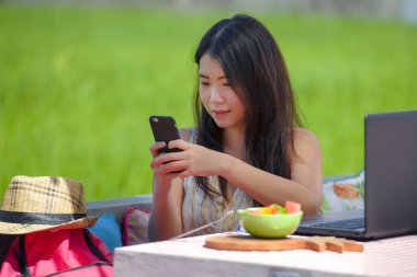 Genç güzel ve mutlu Asya çalışan dijital göçebe kadın açık havada kahve dükkanı masada dizüstü bilgisayar ve cep telefonu Internet online iş ile rahat Korece blogger seyahat 
