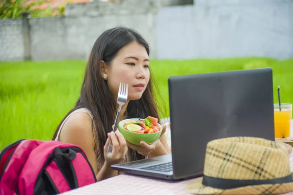 Açık havada çalışan genç çekici ve mutlu Asya Kore Dijital göçebe gibi online sosyal medya blogger seyahat başarı iş sağlıklı salata yemek dizüstü bilgisayar ile rahat