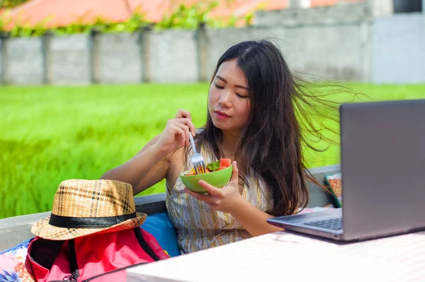 Açık havada çalışan genç çekici ve mutlu Asya Kore Dijital göçebe gibi online sosyal medya blogger seyahat başarı iş sağlıklı salata yemek dizüstü bilgisayar ile rahat