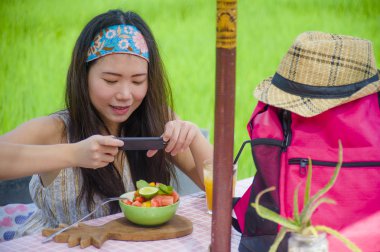 mutlu genç ve oldukça dijital göçebe Asya Çinli kadın alarak resmi meyve salatası ile sağlıklı beslenme ve seyahat blogger gıda inceleme internet sosyal medyada paylaşım için hareket eden telefon
