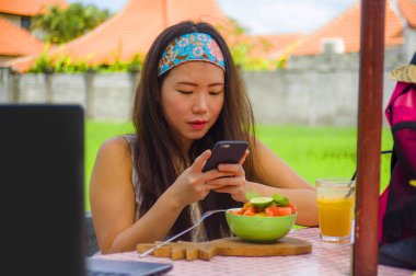Genç mutlu ve meyve salatası cep telefonu ağ ile resmi internet sosyal medyada sağlıklı beslenme ve seyahat blogger gıda alarak çok dijital göçebe Asya Çin kız gözden geçirin