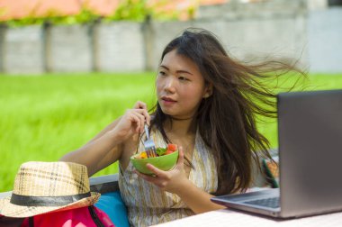 Genç güzel ve mutlu Asya dijital göçebe ya da Çinli turist kız açık havada sağlıklı salata Internet serbest iş iş ve yaşam tarzı kavramı içinde zevk dizüstü bilgisayar ile ağ