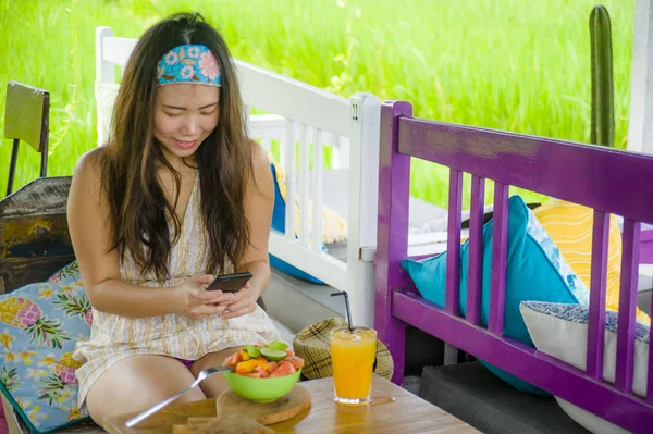 young happy and pretty digital nomad Asian Korean woman taking picture of fruit salad with mobile phone networking on internet social media in healthy nutrition and travel blogger food review