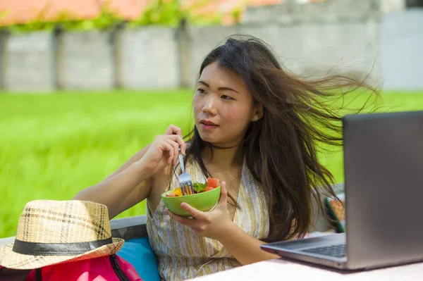Genç güzel ve mutlu Asya dijital göçebe ya da Çinli turist kız açık havada sağlıklı salata Internet serbest iş iş ve yaşam tarzı kavramı içinde zevk dizüstü bilgisayar ile ağ