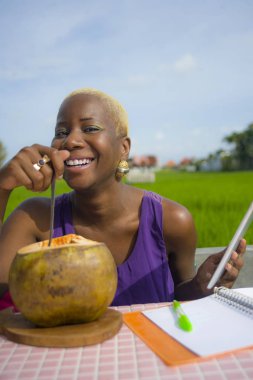 Açık havada içme hindistan cevizinin içine dijital göçebe başarı ve online serbest iş tropikal yerde dijital tablet pad ile çalışan genç çekici ve mutlu başarılı siyah afro Amerikan kadın