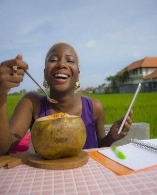 Açık havada içme hindistan cevizinin içine dijital göçebe başarı ve online serbest iş tropikal yerde dijital tablet pad ile çalışan genç çekici ve mutlu başarılı siyah afro Amerikan kadın