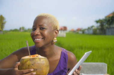 Açık havada içme hindistan cevizinin içine dijital göçebe başarı ve online serbest iş tropikal yerde dijital tablet pad ile çalışan genç çekici ve mutlu başarılı siyah afro Amerikan kadın
