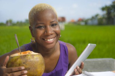 Açık havada içme hindistan cevizinin içine dijital göçebe başarı ve online serbest iş tropikal yerde dijital tablet pad ile çalışan genç çekici ve mutlu başarılı siyah afro Amerikan kadın