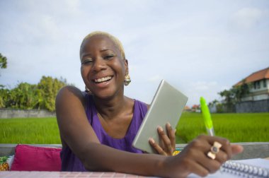 Dijital tablet pad ile açık havada yeşil alan café dijital göçebe başarı ve online serbest iş neşeli gülümseyen üzerinde çalışan genç çekici ve mutlu başarılı siyah afro Amerikalı kadın