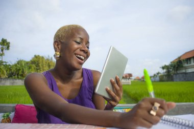 Dijital tablet pad ile açık havada yeşil alan café dijital göçebe başarı ve online serbest iş neşeli gülümseyen üzerinde çalışan genç çekici ve mutlu başarılı siyah afro Amerikalı kadın
