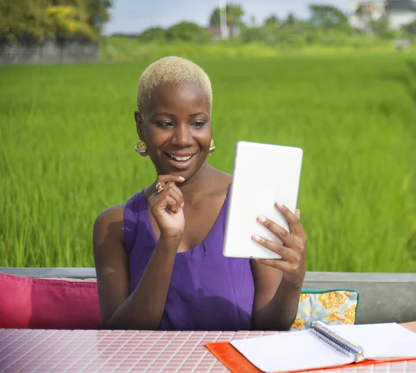 Dijital tablet pad ile açık havada yeşil alan café dijital göçebe başarı ve online serbest iş neşeli gülümseyen üzerinde çalışan genç çekici ve mutlu başarılı siyah afro Amerikalı kadın