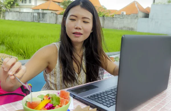 Açık havada dijital göçebe ve Internet serbest iş kavramı sağlıklı salata yemek dizüstü bilgisayar ağ desteği ile çalışan genç güzel ve mutlu Asyalı Koreli kadın